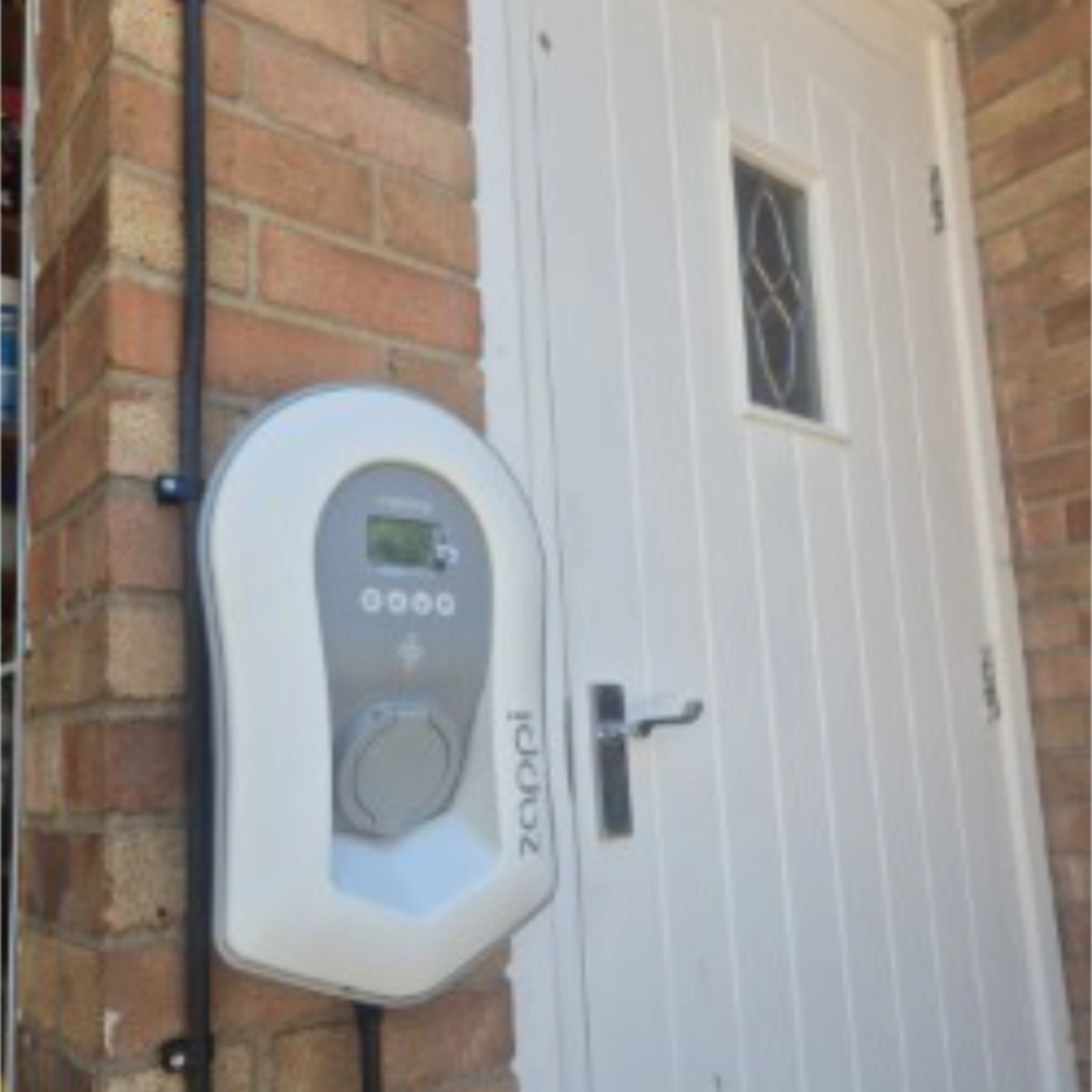 Zappi electric vehicle charger installed on an exterior brick wall beside a white entrance door.